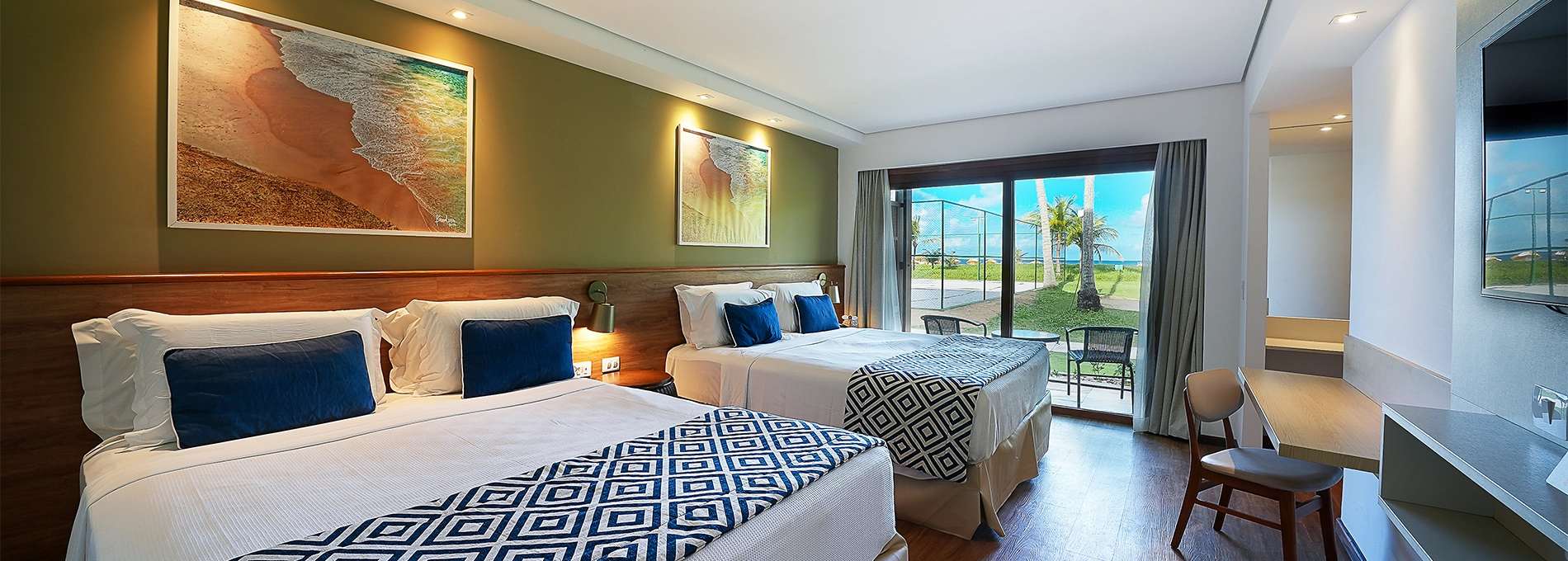 Parte interna da acomodação Praia Frente Mar, com duas camas queen size, quadros decorativos com fotografias de praias de Maragogi e varanda com vista pra praia.