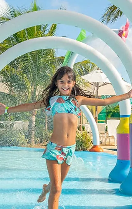 Menina brincando em parque aquático infantil com estruturas coloridas em resort