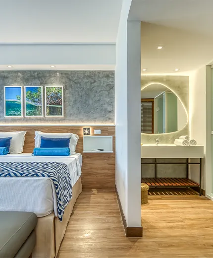 Apartamento Standard Vitória-Régia, uno de los alojamientos en Salinas Maragogi, con cama queen-size, baño y una acogedora decoración con madera, lámparas y una composición de pinturas de las playas de Maragogi.