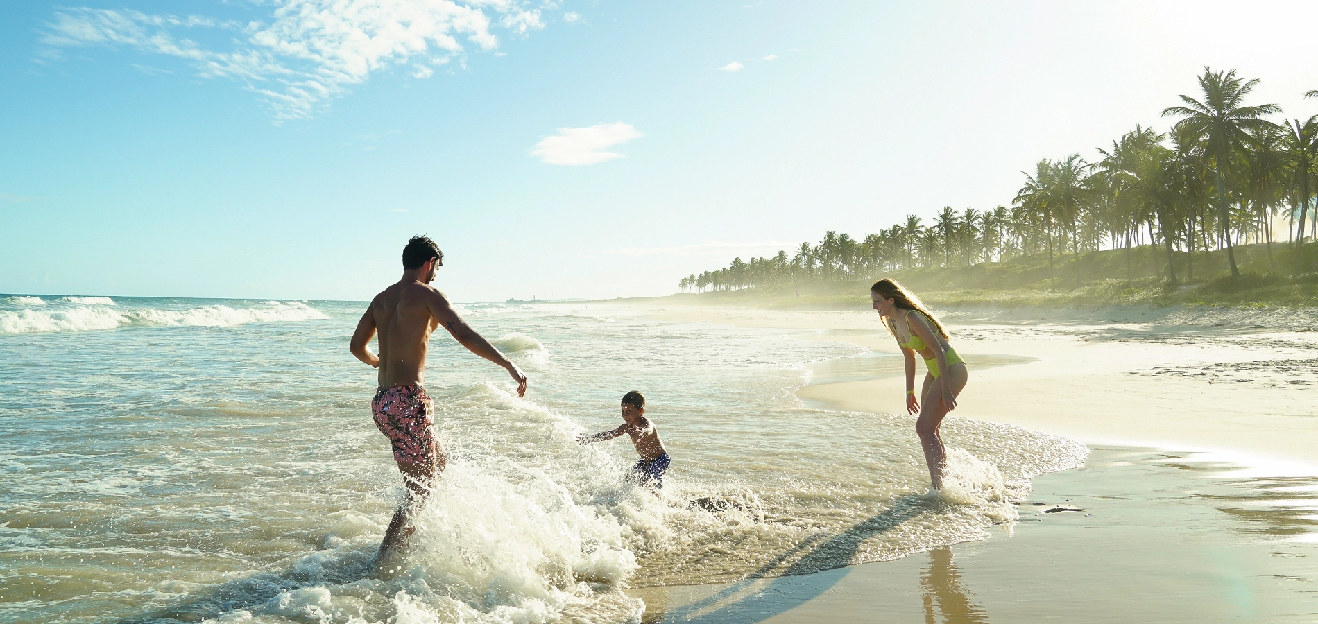 Família feliz brincado nas ondas do mar na Praia do Francês, um dos destinos próximos ao Salinas Maceió, em dia ensolarado.