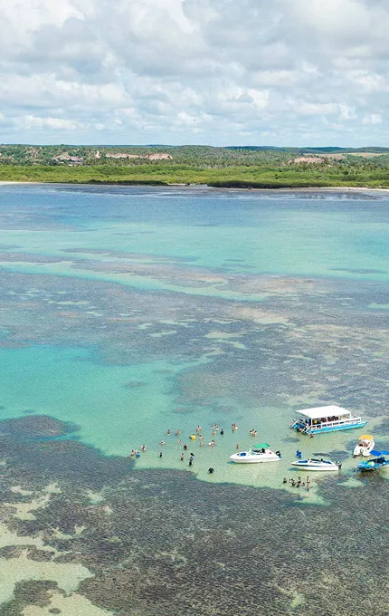 Vista aérea das piscinas naturais de Maceió com águas rasas, recifes de corais e embarcações turísticas