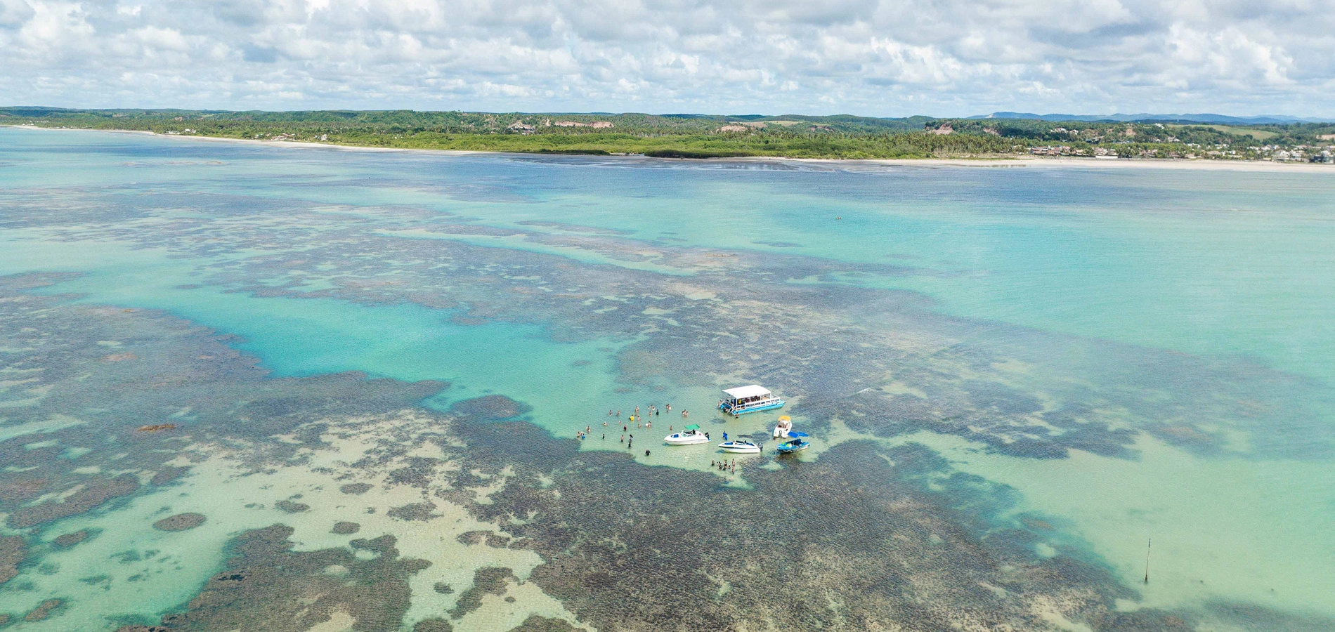 Vista aérea das piscinas naturais de Maceió com águas rasas, recifes de corais e embarcações turísticas