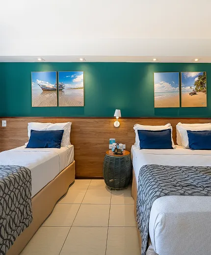 Quarto Apartamento Standard no Salinas Maceió com cama casal e cama solteiro, decoração praiana com parede verde e quadros pendurados na parede, e espaço confortável pra família.