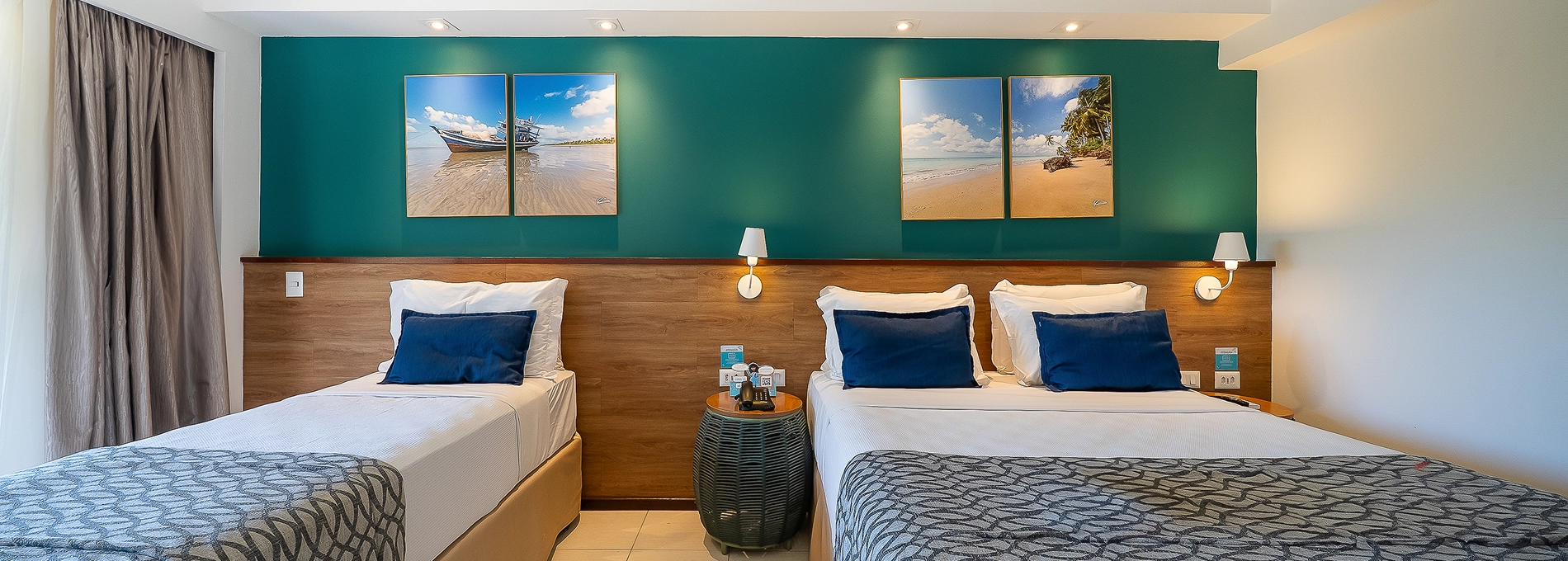 Quarto Apartamento Standard no Salinas Maceió com cama casal e cama solteiro, decoração praiana com parede verde e quadros pendurados na parede, e espaço confortável pra família.
