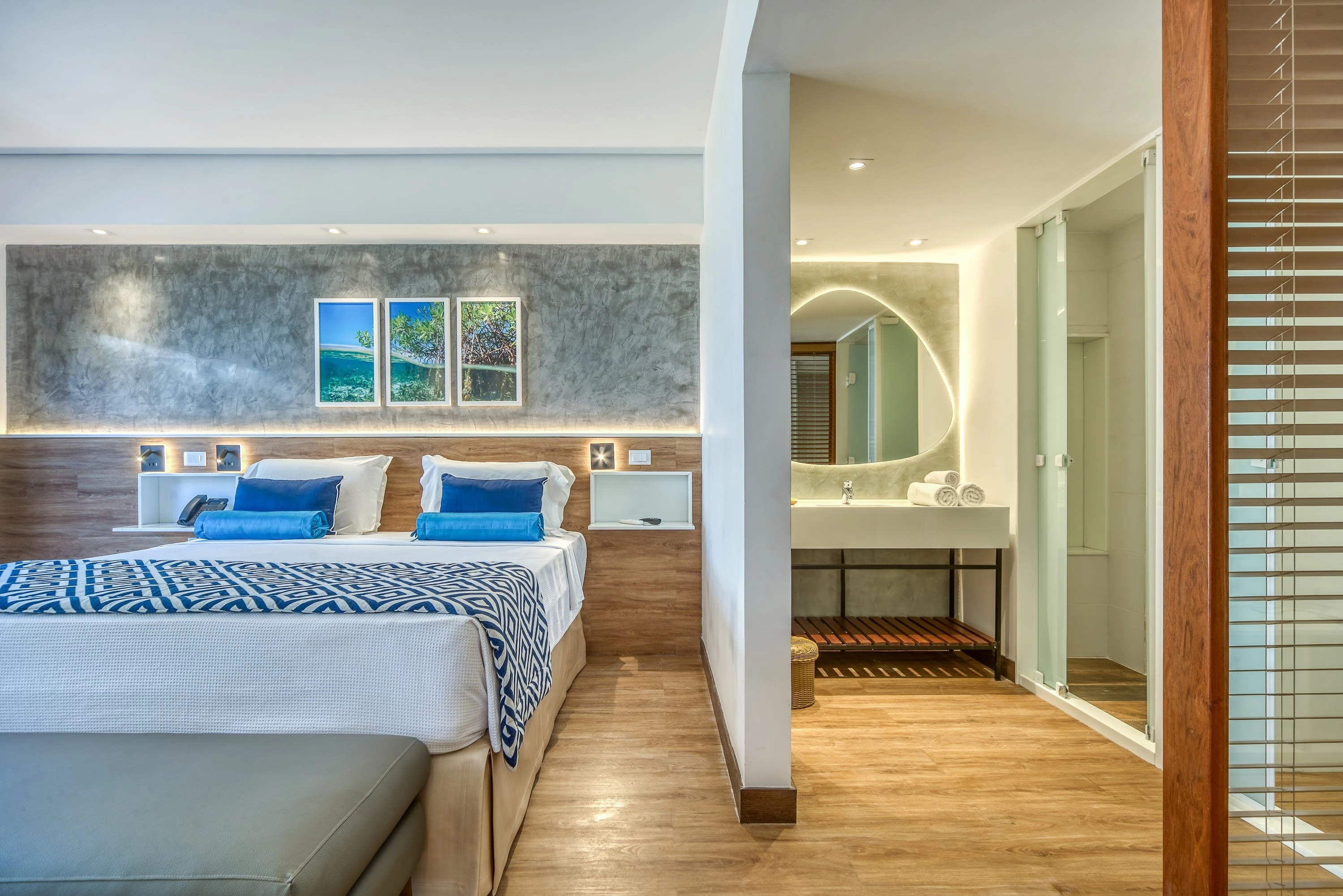 Apartamento Standard Vitória-Régia, uma das acomodações do Salinas Maragogi, com cama uma queen size, banheiro e decoração aconchegante composta por madeira, luminárias e uma composição de quadros de praias de Maragogi.