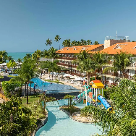 Vista do resort Salinas Maceió com as piscinas, área recreativa para crianças e a praia ao fundo.