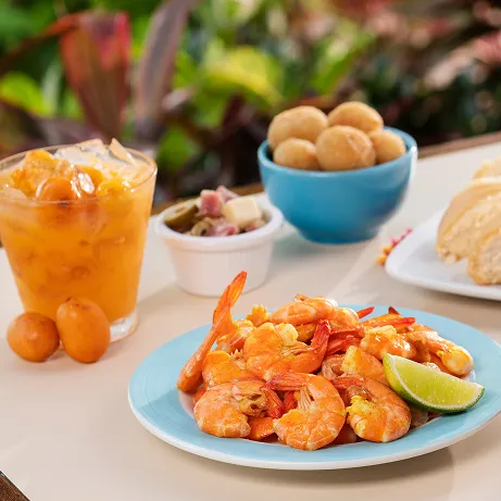 Mesa ao ar livre com cerveja Budweiser, camarões, caipirinha de uvaia, pães de queijo e acompanhamentos