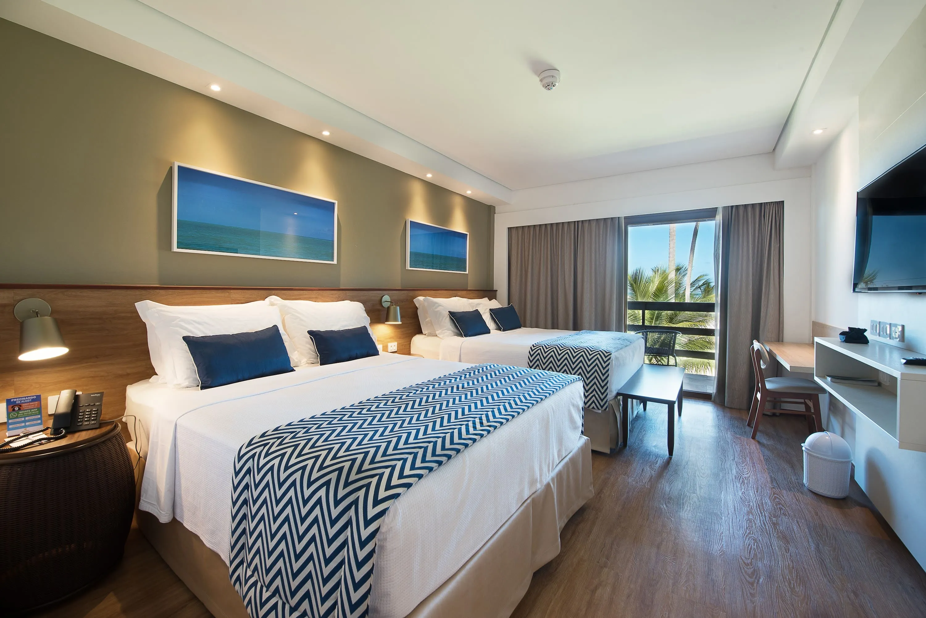 Detalles del apartamento frente a la playa, con dos camas queen, mesa y sillas, pantalla de TV por cable, decoración acogedora, fotografías enmarcadas de las playas de Maragogi y balcón con vista al mar.