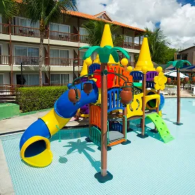 Crianças e adultos brincam na piscina infantil do Salinas Maceió, que possui um grande toboágua verde e brinquedos coloridos dentro da piscina de água azul, com os prédios do resort ao fundo.