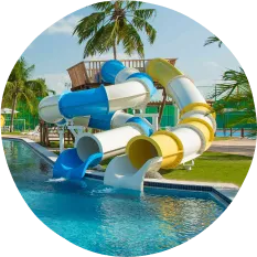 Vista de parque aquático com piscina em curva, toboáguas coloridos, espreguiçadeiras e palmeiras tropicais sob céu azul.