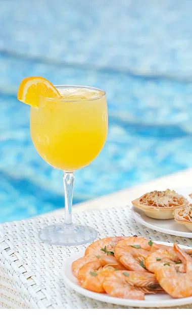 Bebida al lado de bocadillos sobre una mesa blanca cerca de na piscina.