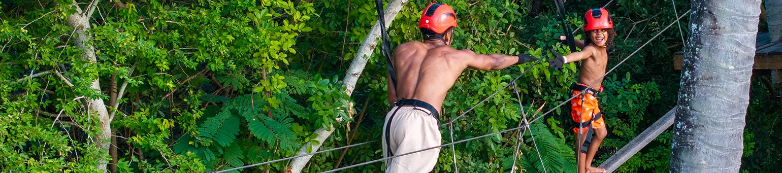 Criança e adulto praticando arvorismo em meio à natureza dentro de resort.