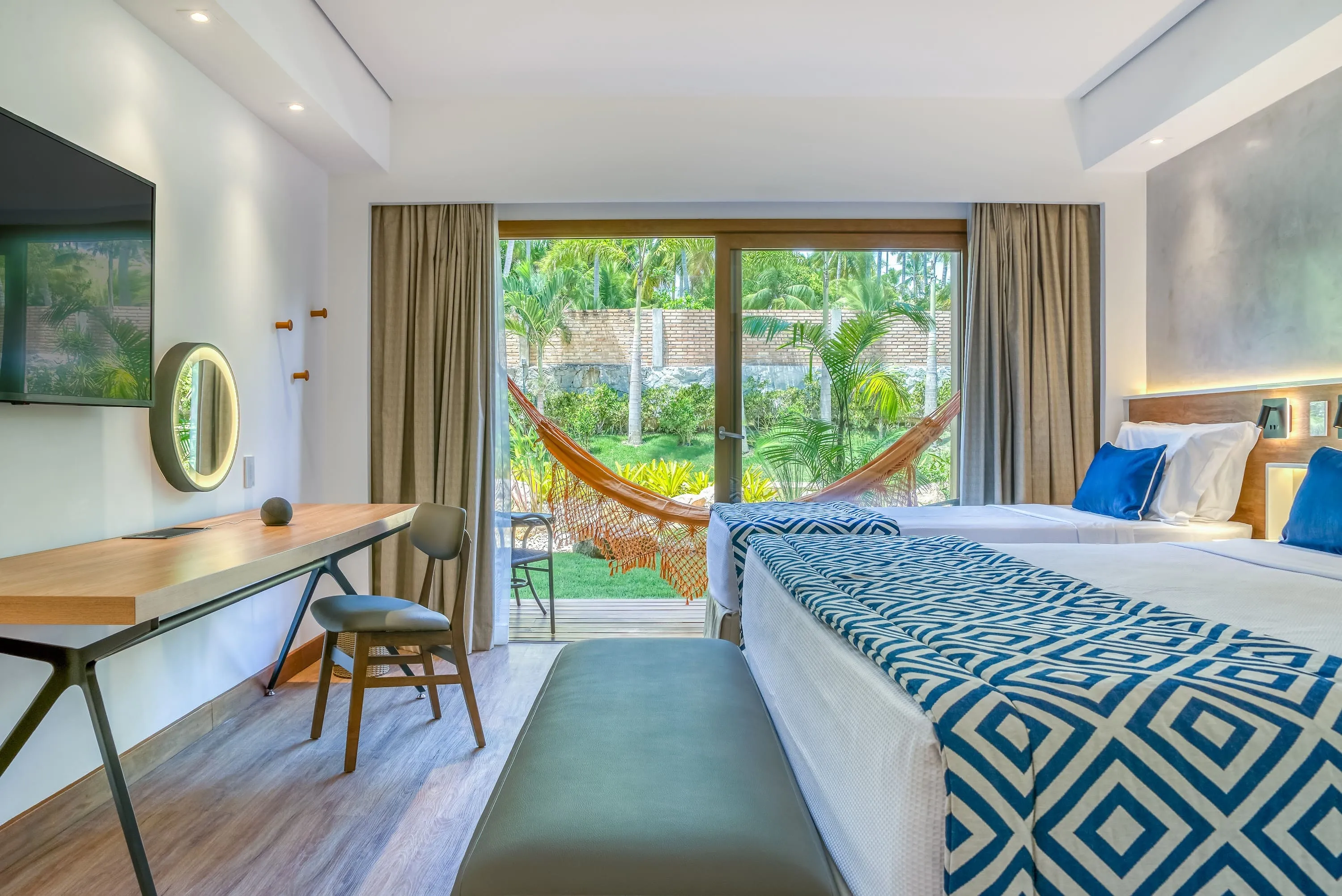 Detalles del área principal del alojamiento Standard Vitória-Régia, con cama queen-size y cama individual, mesa y silla, panel con TV por cable, espejo redondo con iluminación, decoración acogedora y balcón con hamaca. El apartamento tiene vista al jardín.
