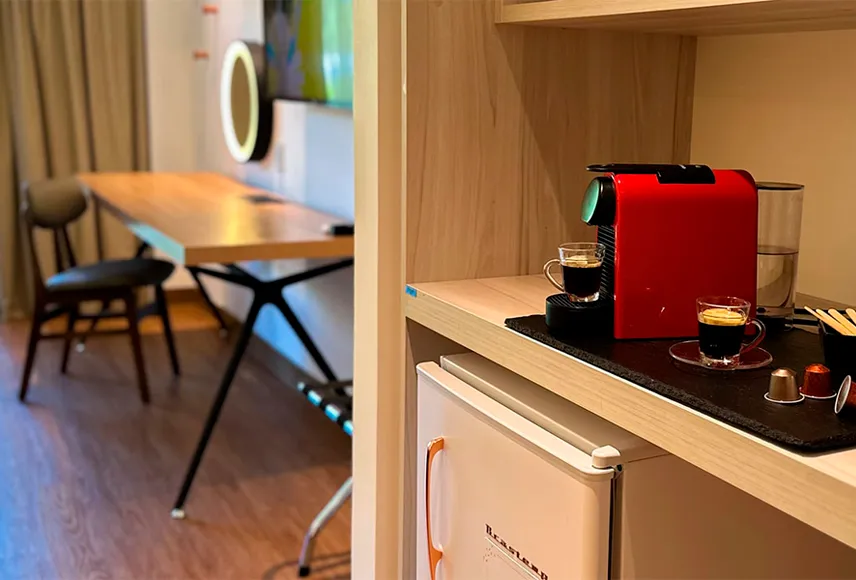 Baño en el Standard Vitória-Régia, con un espejo de forma orgánica sobre el lavabo, toallas dispuestas en la encimera y colgadas junto al lavabo, un espejo de aumento, secador de pelo, decoración y artículos de tocador L'Occitane.