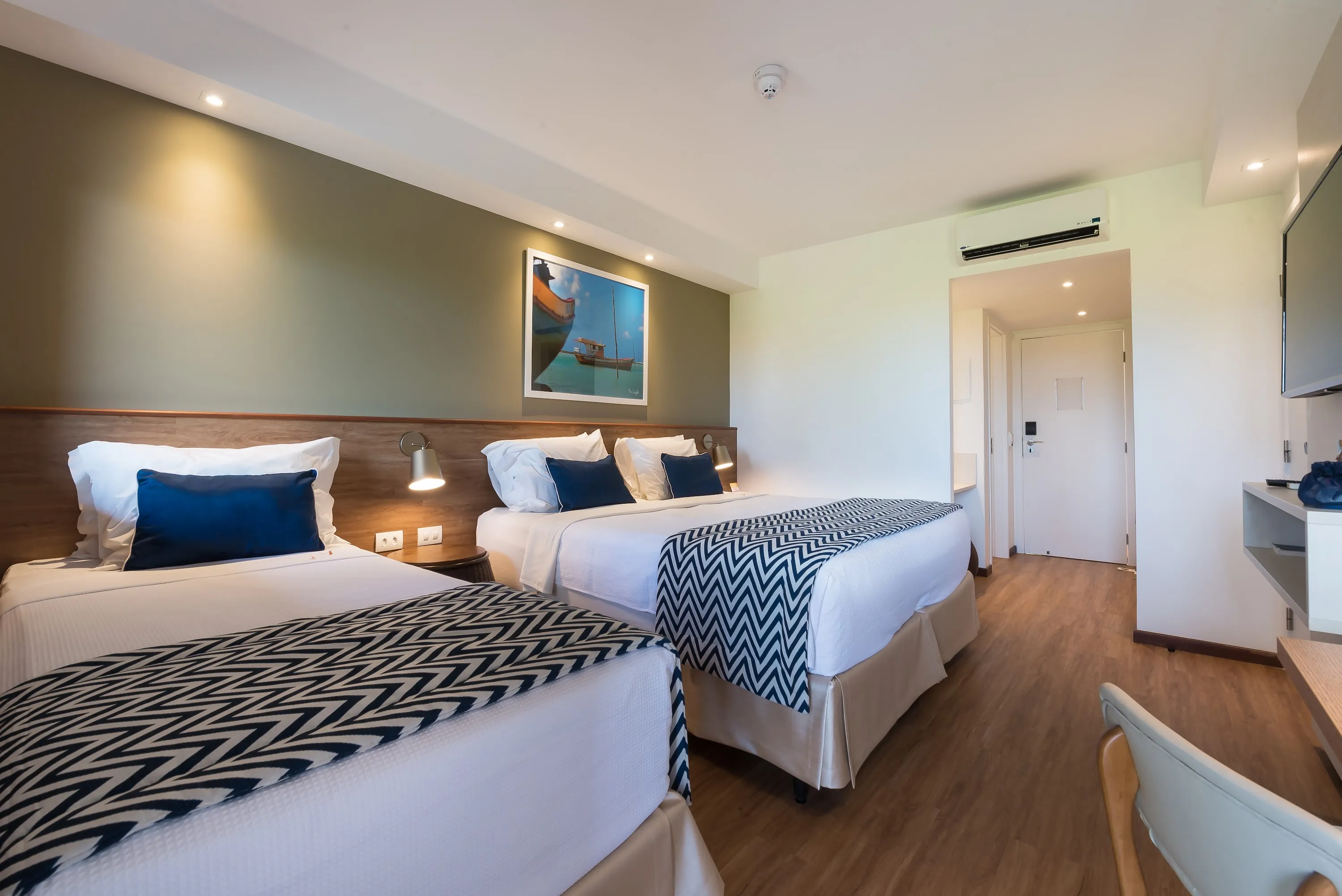 Apartamento estándar, uno de los alojamientos en Salinas Maragogi, con una cama queen y una cama individual, televisor, mesa y una decoración acogedora con detalles de madera, lámparas y un cuadro de la playa de Maragogi.