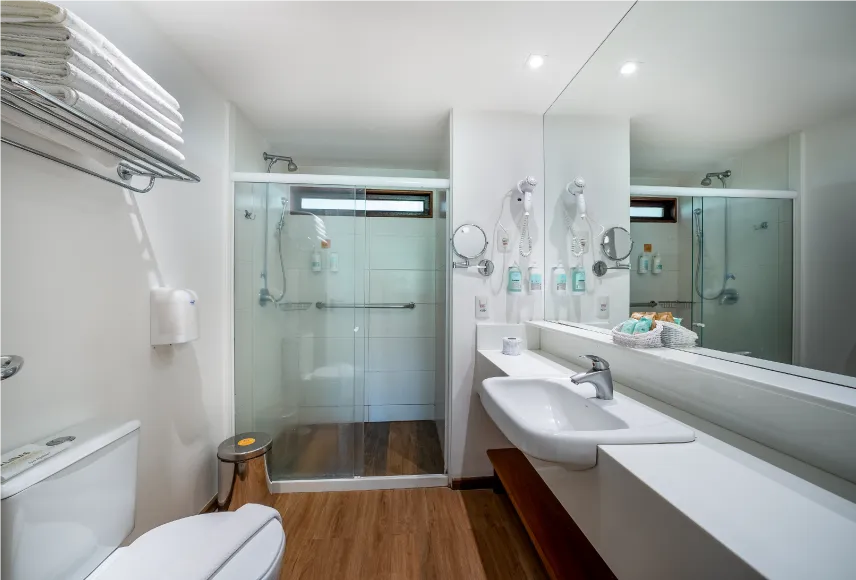 Baño de la Suite Familiar con zona de baño, inodoros, ducha con control de temperatura, decoración, artículos de aseo O Boticário, toallas, un espejo grande y secador de pelo.