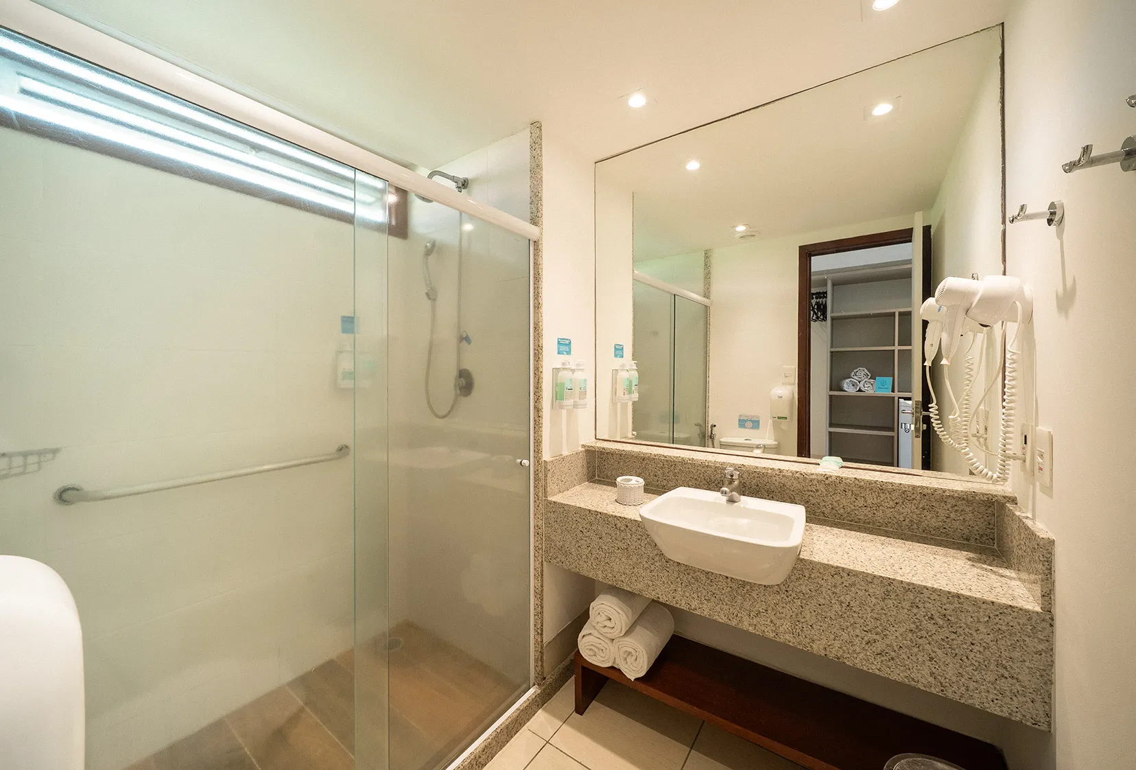 Banheiro da acomodação Superior, com área de banho e chuveiro com regulagem para temperatura, pia, toalhas, secador de cabelo e amenities O Boticário.