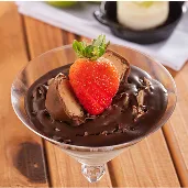 Taça de sobremesa com chocolate e morango, acompanhada de outras opções doces ao fundo