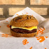 Prato com hambúrguer artesanal com queijo, sobre mesa de madeira. Ao fundo, parede de tijolos.