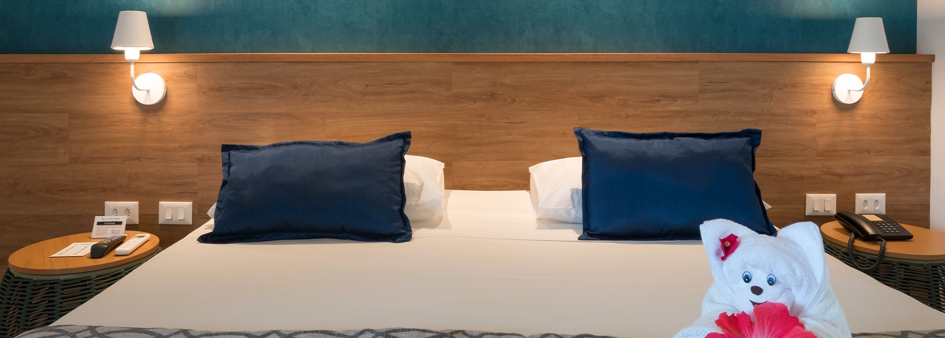 Acomodação Standard, uma das acomodações do Salinas Maceió All Inclusive Resort, com uma cama queen size aconchegante no centro, painel de madeira atrás da cama com duas luminárias e duas mesas de cabeceira, uma em cada lado da cama.