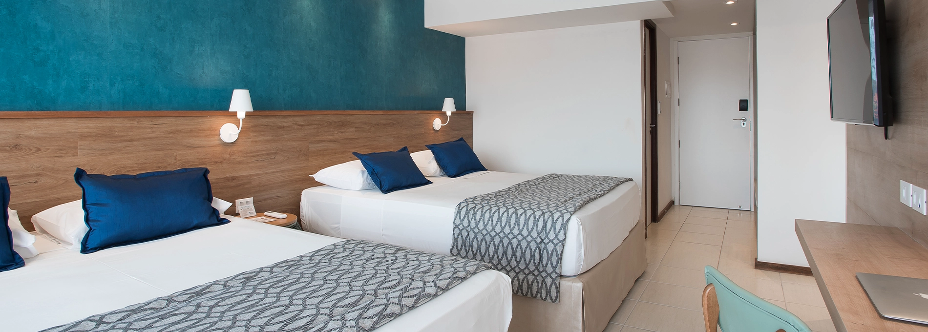 Acomodação Superior, do Salinas Maceió All Inclusive Resort, com duas camas queen size, painel de madeira à frente, com TV a cabo, mesa e cadeira e ar condicionado
