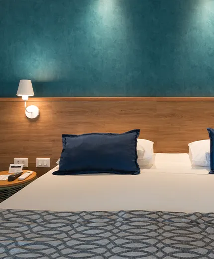 Acomodação Standard, uma das acomodações do Salinas Maceió All Inclusive Resort, com uma cama queen size aconchegante no centro, painel de madeira atrás da cama com duas luminárias e duas mesas de cabeceira, uma em cada lado da cama.