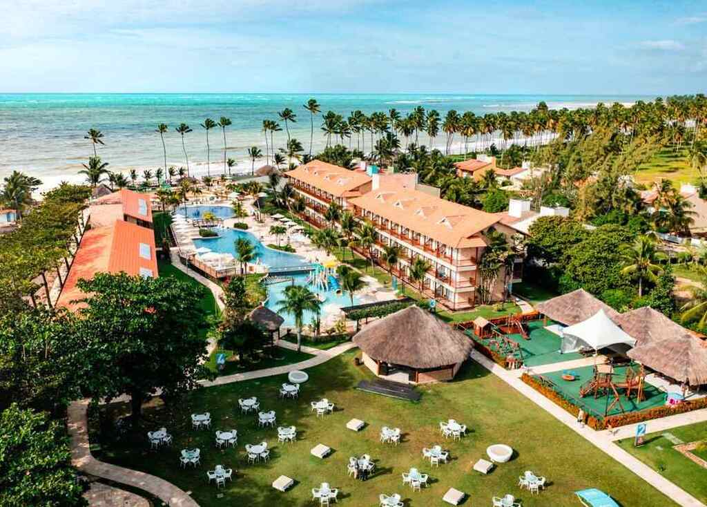 Vista aérea do Resort Salinas Maceió com piscina, áreas verdes, cabanas e acesso ao mar azul na costa de uma praia tropical, cenário de férias perfeito.