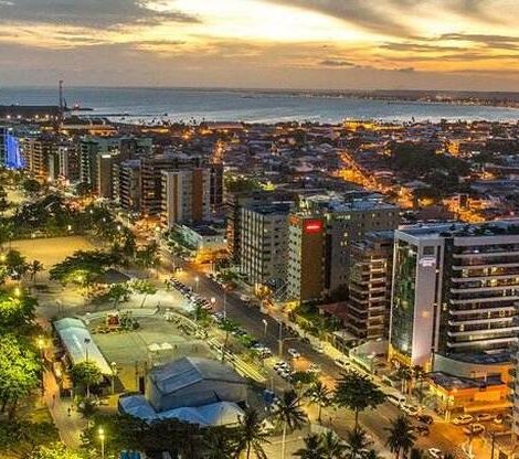 Vista panorâmica da orla de Maceió ao entardecer, com praia, prédios modernos e linhas de iluminação que destacam a elegância urbana.