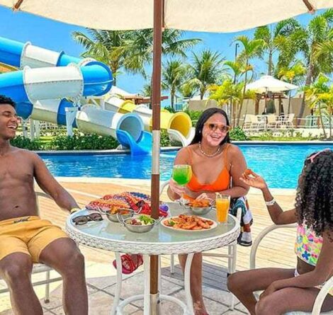 Família aproveitando dia ensolarado na piscina com área de diversão aquática, com adultos e uma criança sorrindo e confraternizando, ambiente relaxante e paradisíaco.