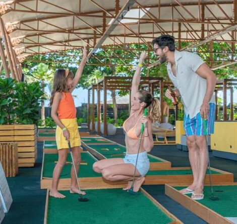 Pais e criança em viagem para família se divertindo juntos em uma área de mini golfe ao ar livre.