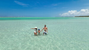Uma família na Praia de Xaréu em águas cristalinas e com maré baixa. O céu está azul sem nuvens.