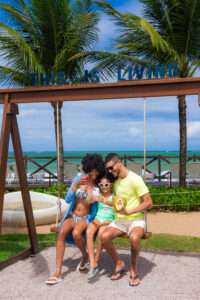 Família tirando foto em balanço instagramável no Salinas Maceió. A filha está no meio dos pais tirando uma selfie com eles, sentados no balanço.