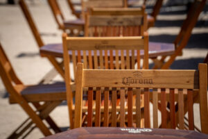 Meses e cadeiras de madeira com a logo da cerveja Corona.
