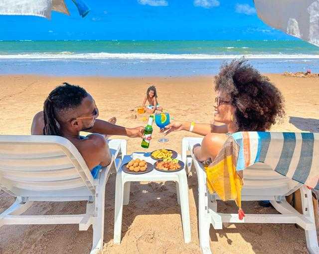 Casal e filho sentados na beira do mar, curtindo a praia de Ipioca, em frente ao Salinas Maceió.