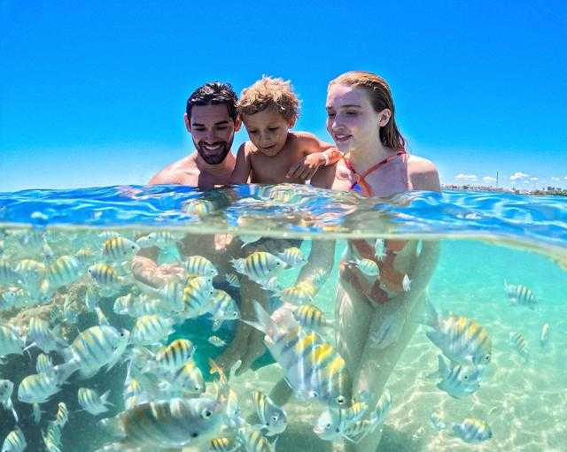 Casal e filho nadando com peixinhos nas piscinas naturais da praia de Pajuçara.