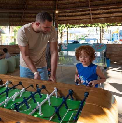 salao de jogos Família jogando pebolim no salão de jogos, tem algumas crianças no video-game ao fundo.