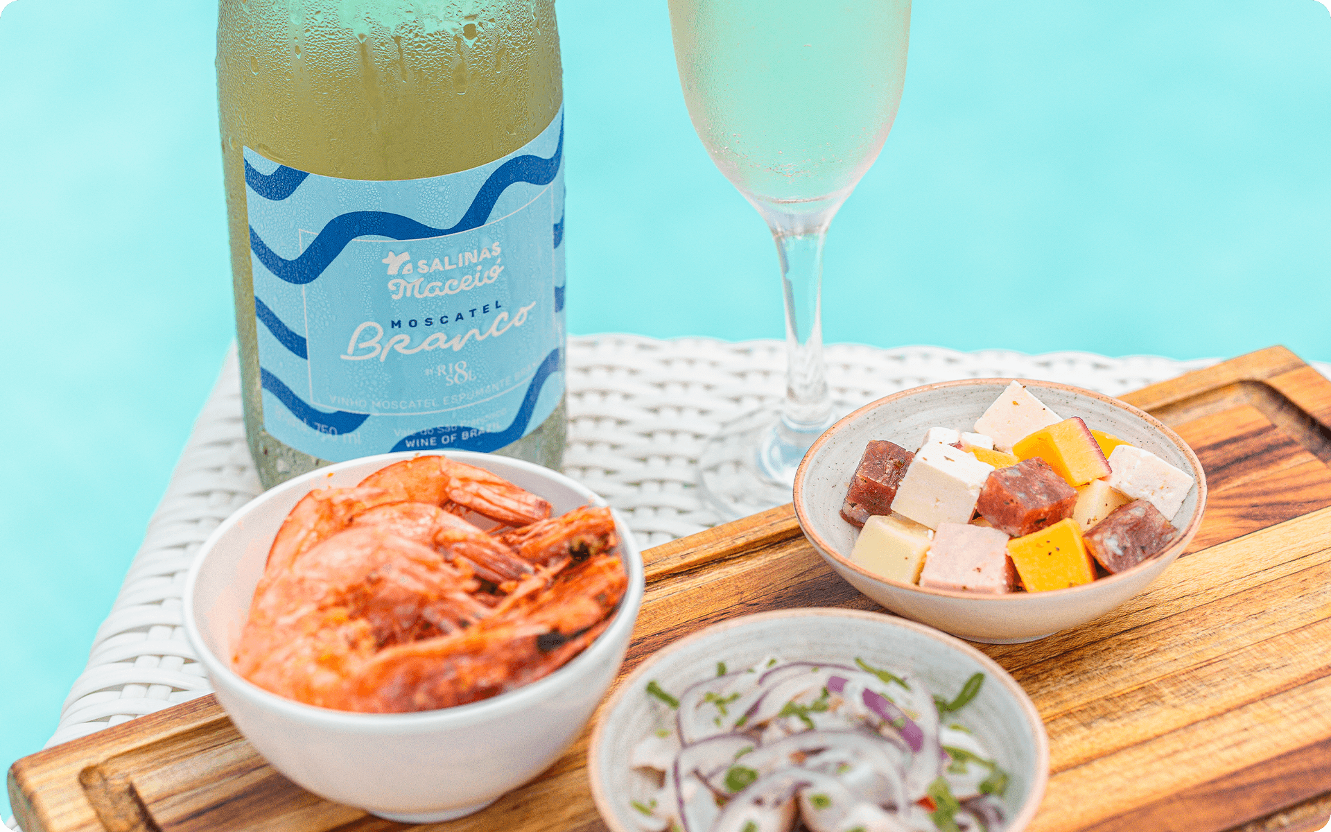 A garrafa de Moscatel do Salinas Maceió com taça ao lado. Petiscos como camarão, ceviche e queijos variados a beira da piscina.