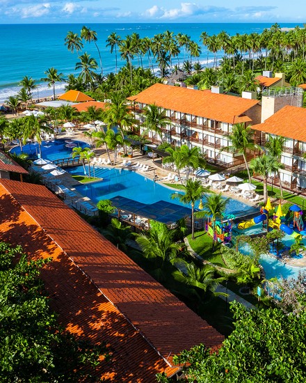A estrutura completa do Salinas Maceió All Inclusive Resort vista do alto. Vista aérea do resort Salinas Maceió. A área de lazer possui piscinas interligadas e escorregadores. Ao fundo, diversos coqueiros e a praia com o mar azul.