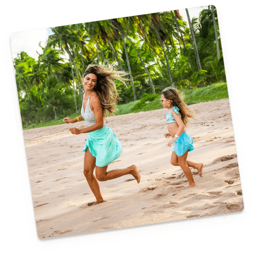 mãe e filha brincando na praia Mãe e filha brincando na praia com coqueiros e um céu azul ao fundo.