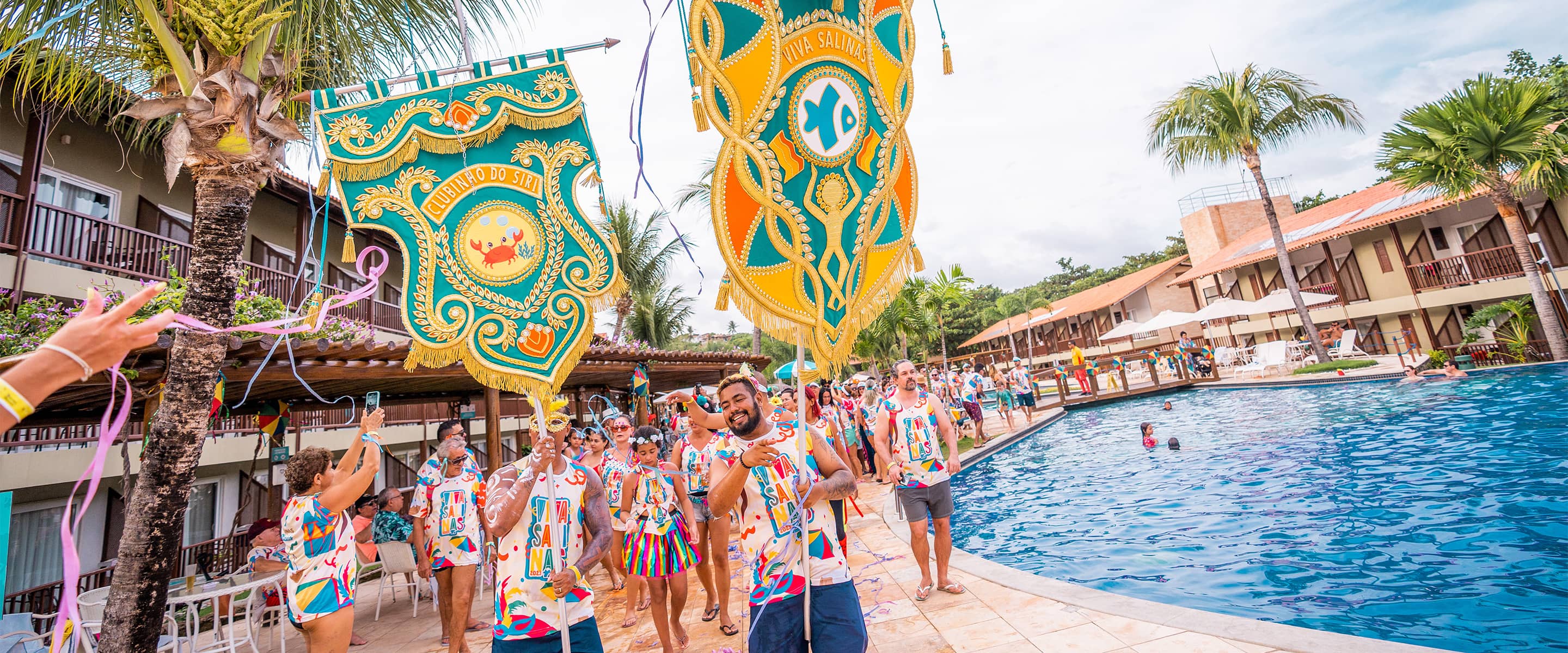 Pessoas acompanham estandarte do bloco e vestidas com o abadá do bloco Viva Salinas enquanto caminham ao redor da piscina do Salinas Maceió.