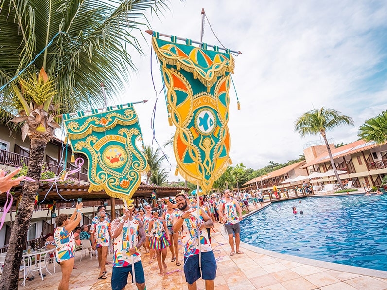 Pessoas acompanham standart do bloco e vestidas com o abadá do bloco Viva Salinas enquanto caminham ao redor da piscina do Salinas Maceió.