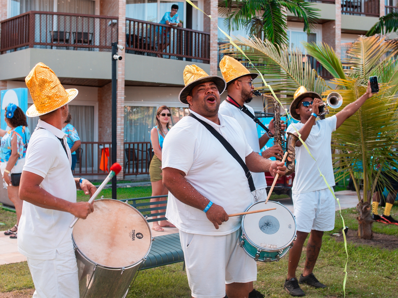 Orquestra musical na área de lazer, comandando a diversão no carnaval Salinas Maceió. São 4 integrantes de camisa branca, cada um está com seu instrumento tocando.