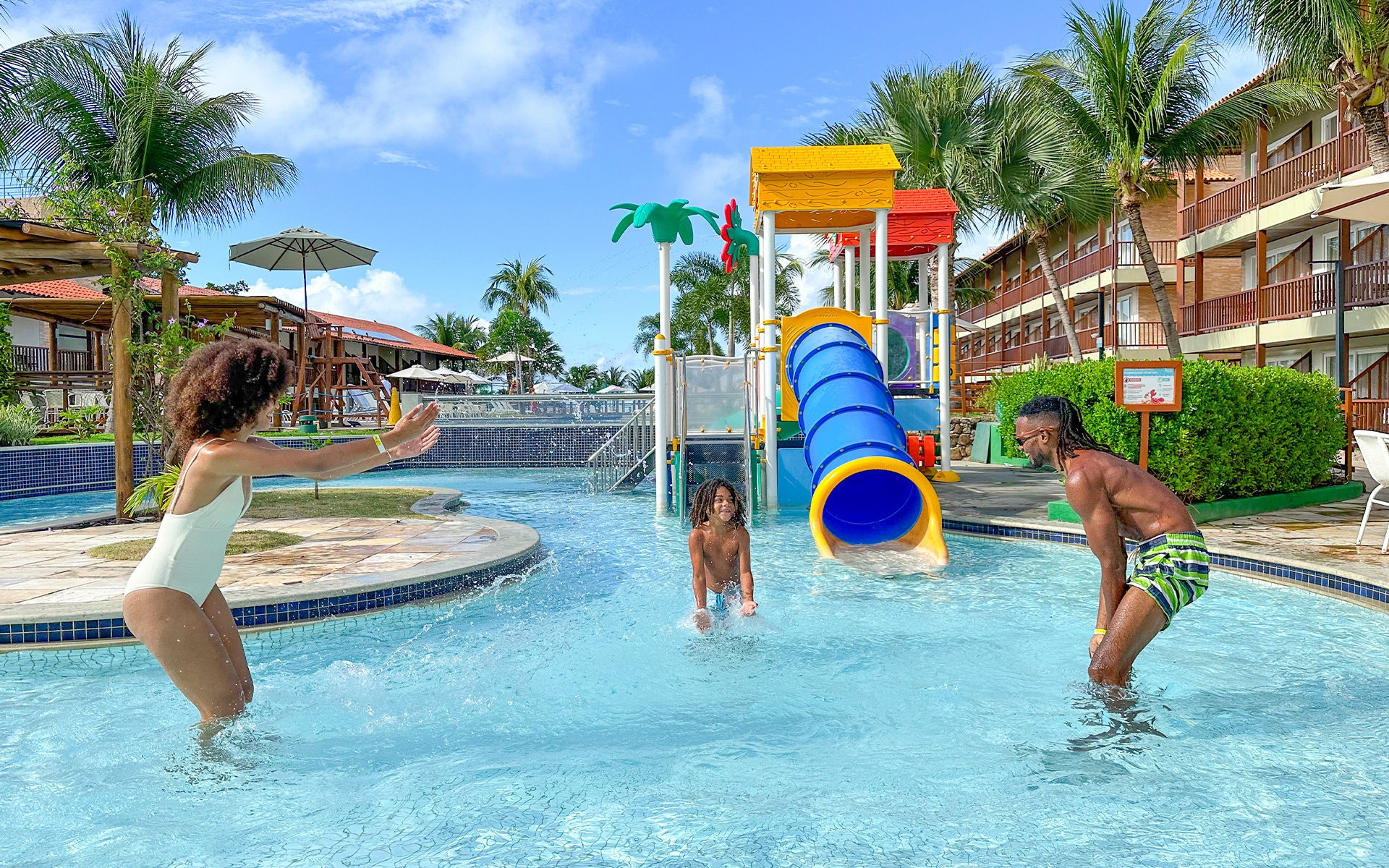 Família se divertindo na piscina infantil do Salinas Maceió, com brinquedos aquáticos coloridos, crianças brincando e estrutura ao fundo.