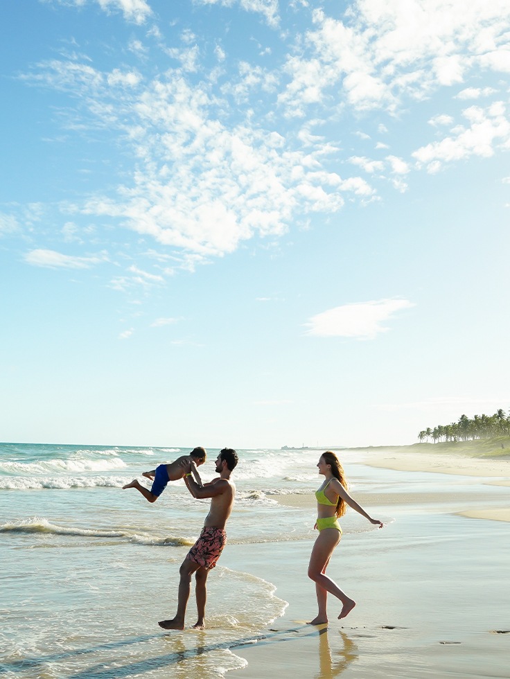 Família se divertindo na Praia do Francês, com mar azul, areia clara e céu sem nuvens.
