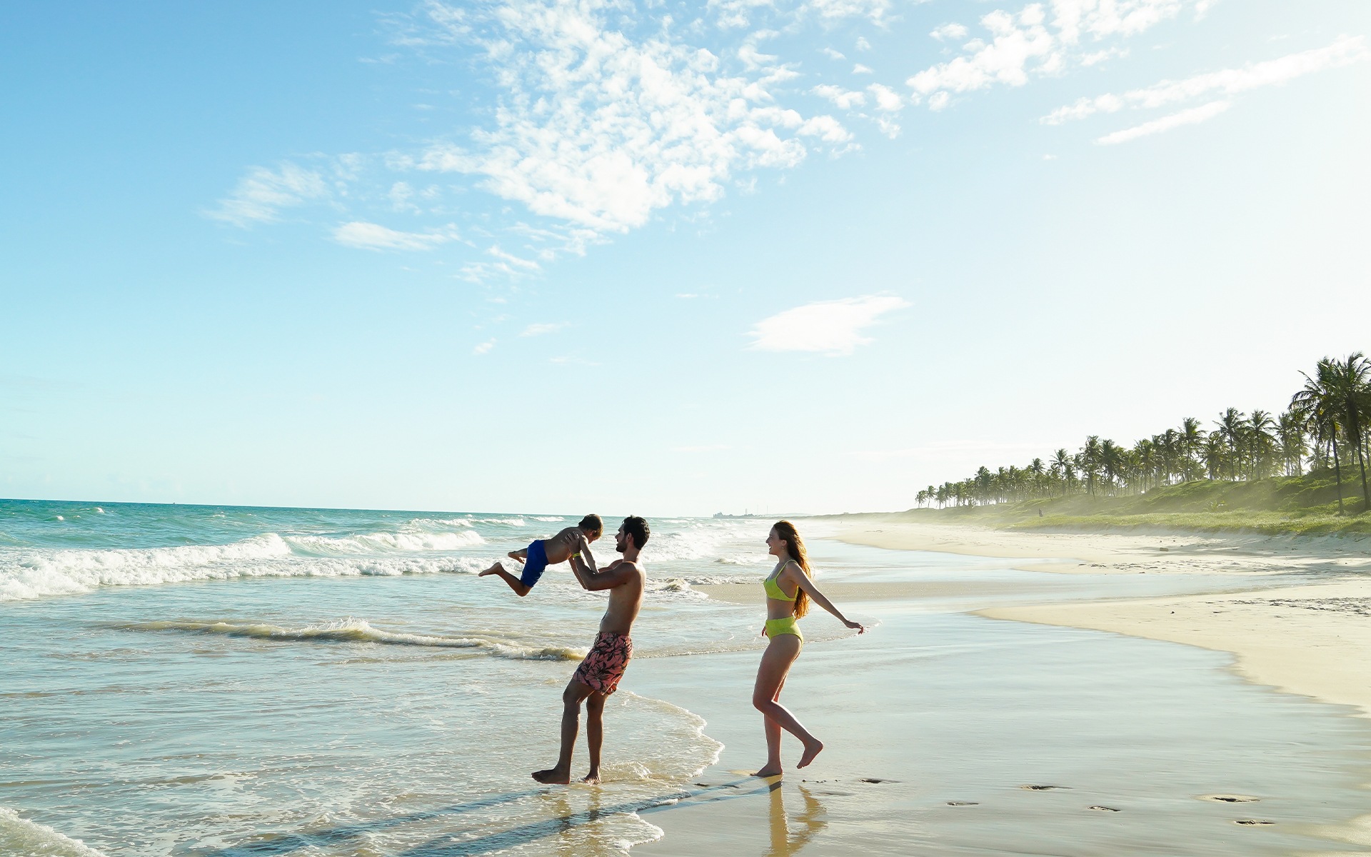 Família se divertindo na Praia do Francês, com mar azul, areia clara e céu sem nuvens.