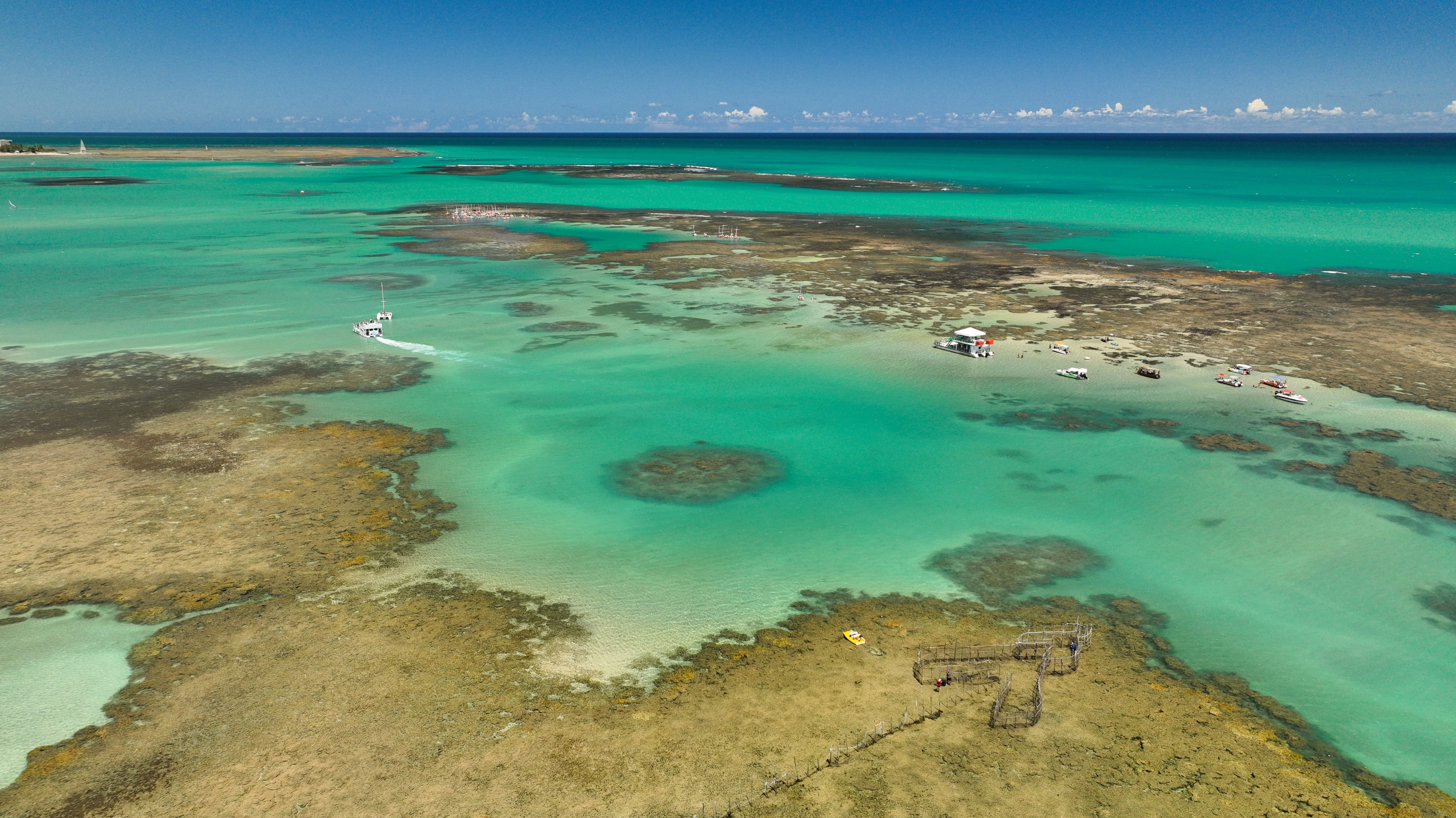 Barcos de passeio sob as águas azul turquesa das piscinas naturais de Maceió