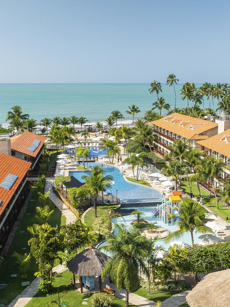 É no Salinas Maceió All Inclusive Resort onde as férias de 2027 começam Vista aérea do Salinas Maceió All Inclusive Resort apresentando o complexo de piscinas, parque aquático infantil, área de lazer, cercados por coqueiros e vegetação litorânea, além da praia ao fundo.