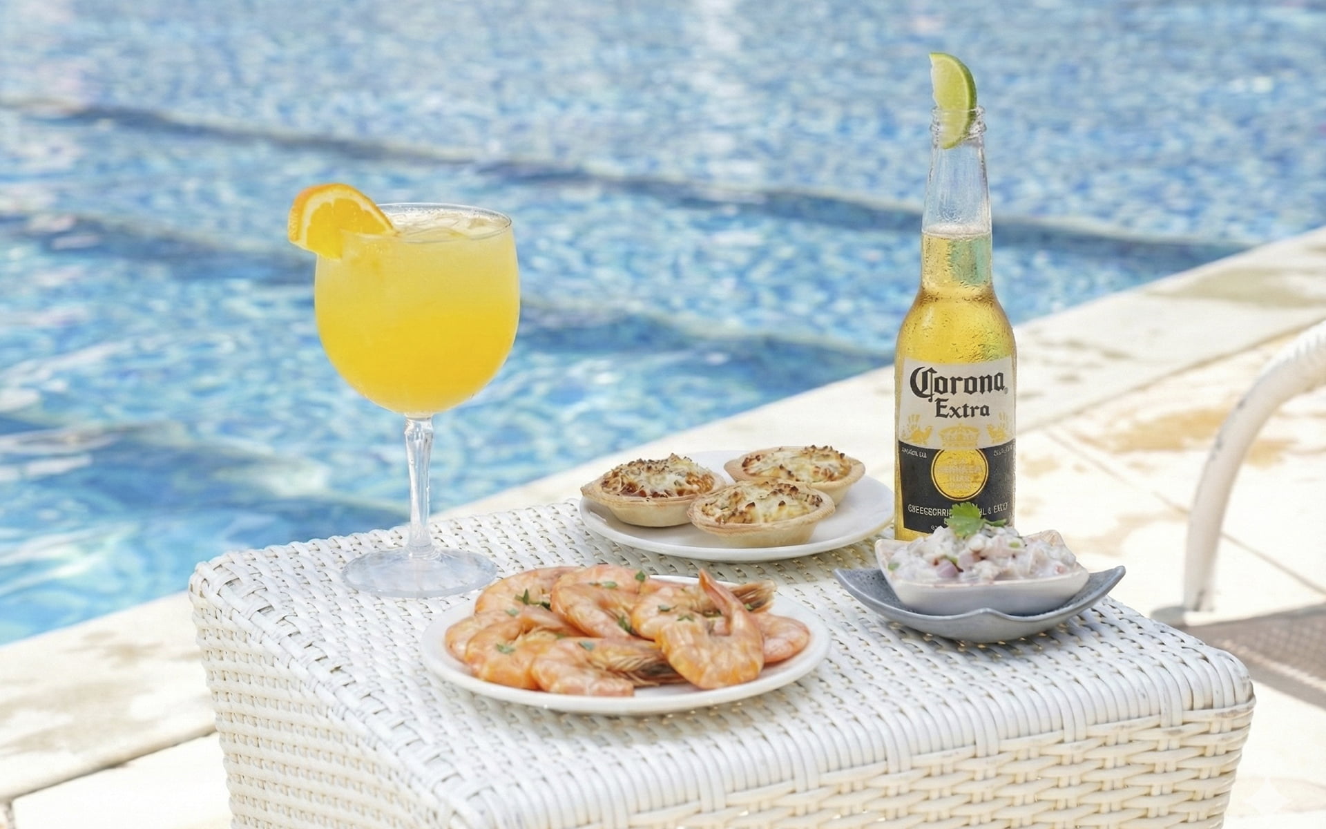 Sabores que combinam com o verão 2027. Mesa à beira da piscina do Salinas Maceió com drink cítrico, cerveja Corona gelada, camarões, tortinhas gratinadas e ceviche.