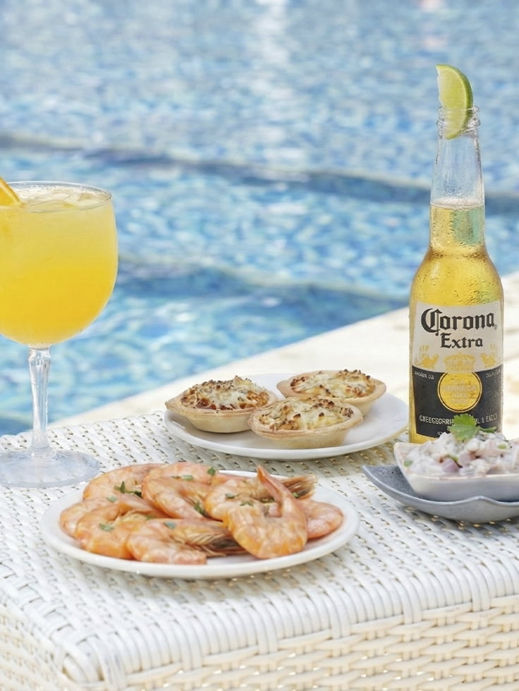 Sabores que combinam com o verão 2027. Mesa à beira da piscina do Salinas Maceió com drink cítrico, cerveja Corona gelada, camarões, tortinhas gratinadas e ceviche.