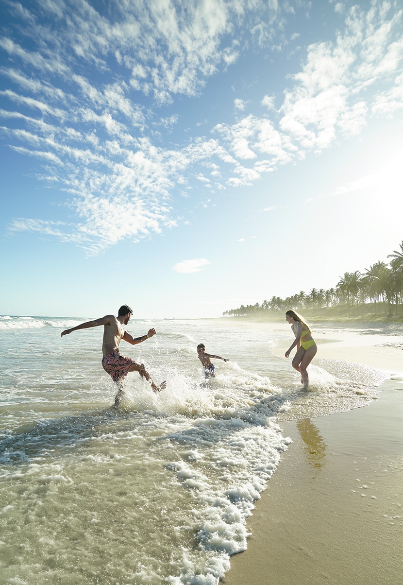 Casal e criança brincando na praia do Salinas Maceió, em dia ensolarado e com coqueiros ao fundo Casal e criança brincando na praia do Salinas Maceió, em dia ensolarado e com coqueiros ao fundo